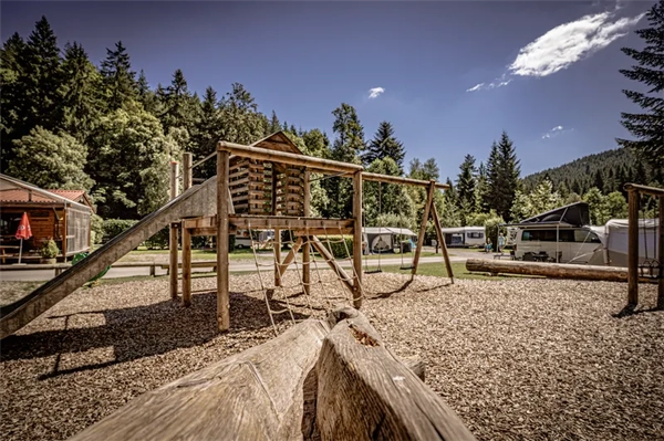 Spielplatz mit Rutsche und Schaukeln auf dem Campingplatz, im Hintergrund sind Stellplätze und Bewaltete Berge
