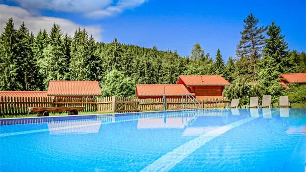 Natur-Camping Langenwald im Schwarzwald 5 Schönes Schwimmbecken mit Sonnenliegen mit aussiecht auf die mit Tannen bewachsenen Berge und Unsere Ferienhäuser im Camping langenwald